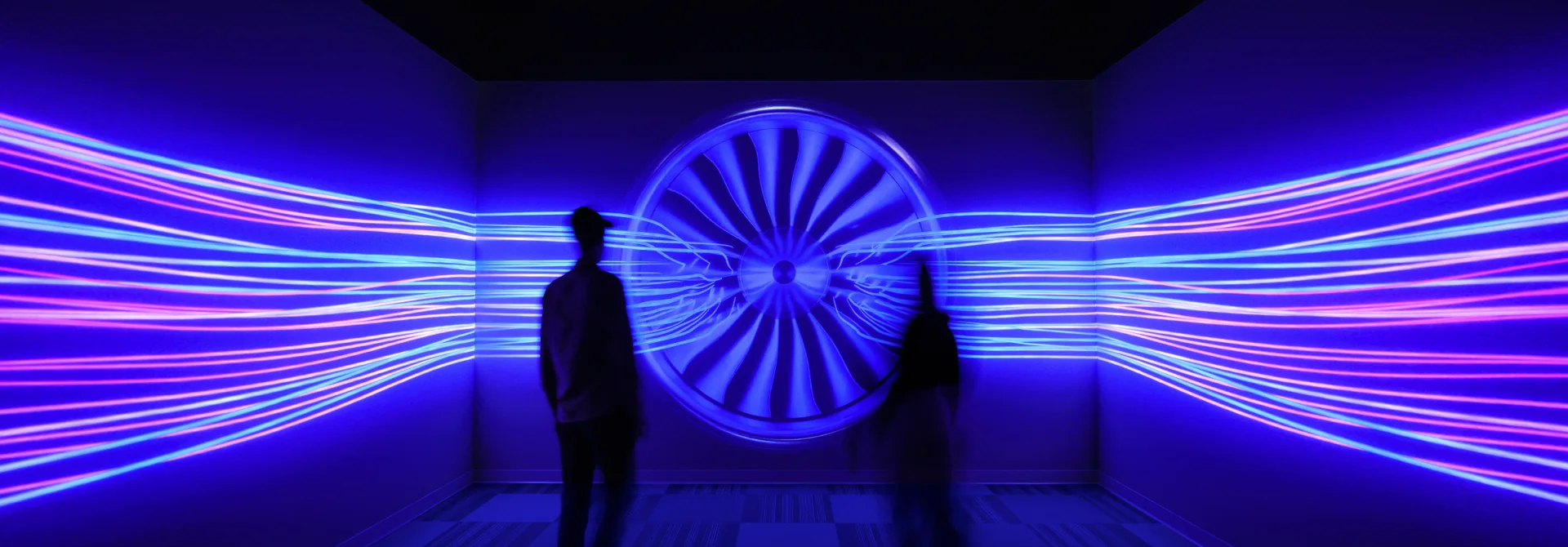 Two people stand in front of a projected airplane engine, with flow patterns extending to either side.